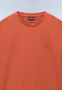T-shirt a maniche corte e colletto rotondo in cotone color arancio bruciato, con un piccolo logo ricamato sul lato sinistro del petto.