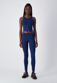 Marineblauwe sport crop top en legging gemaakt van rekbaar materiaal, gecombineerd met zwarte sportschoenen met rode accenten en een gestructureerde zool.