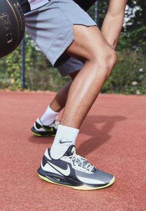 Person trägt schwarze und weiße Nike-Sneaker und weiße Socken, dribbelt mit einem Basketball auf einem Außenplatz.