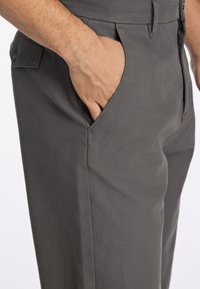 Pantalons en tissu gris avec poches latérales, texture lisse et coupe ajustée, avec des détails de couture visibles.