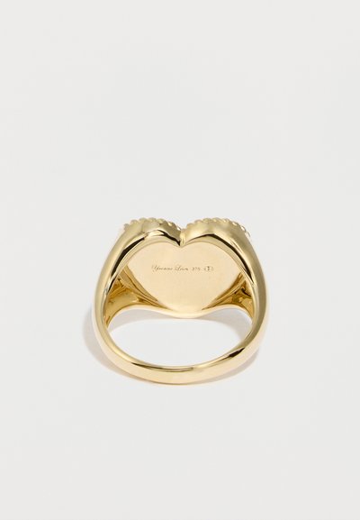Χρυσό δαχτυλίδι με σχέδιο καρδιάς, με γυαλιστερό φινίρισμα, κυρτό σχήμα και μικρές διακοσμητικές κυματιστές λεπτομέρειες. Χαραγμένο λογότυπο στην εσωτερική πλευρά της μπάντας.