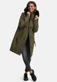 Olive green parka with a detachable black fur-lined hood, zip closure, side pockets, and adjustable drawstring hem. Paired with black sneakers.