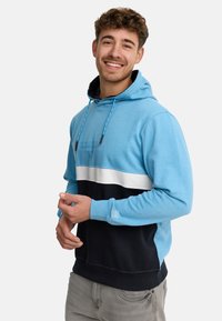 Sweat-shirt à capuche bleu clair, avec une bande blanche sur la poitrine et un bas bleu foncé. Il dispose de cordons de serrage ajustables et de poignets côtelés.