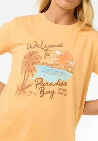Korte mouwen, gele katoenen t-shirt met een afbeelding van palmbomen, een zonsondergang en water, met de tekst "Welkom in Paradise Bay" in bruin.