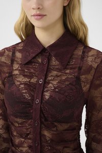 Bordeaux kanten blouse met een transparante overlay, voorzien van een kraag, knoopsluiting, bloemmotieven en textuurstof.