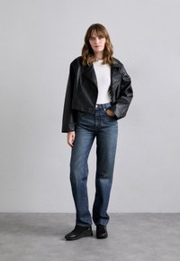 Svart lær cropped jakke over en hvit topp, sammen med lyseblå straight-leg jeans og svarte slip-on sko. Glatte teksturer og klassisk passform.