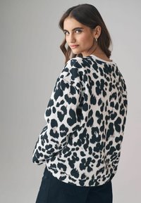 Felpa bianca con stampa leopardata nera, caratterizzata da una vestibilità comoda, scollo a giro e maniche lunghe, abbinata a pantaloni scuri.