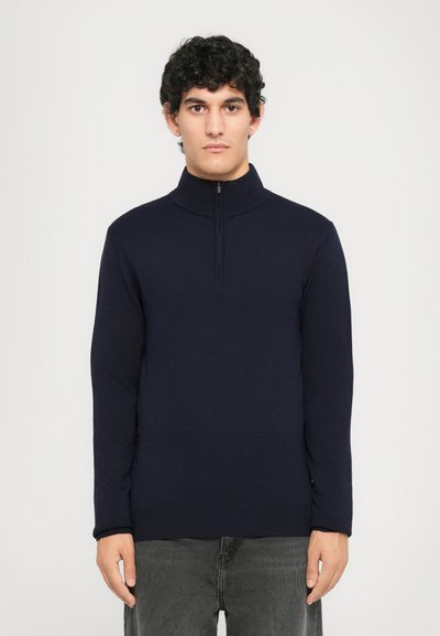 Suéter de punto azul marino con un alto cuello y diseño de medio cierre. Presenta mangas largas y puños y dobladillo acanalados. Textura suave.