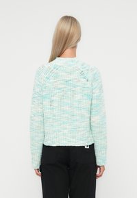 Heklet genser i mintgrønn og hvit, med ribbestrikket kant, rund halslinning og lange ermer med lette raglan-sømmer.