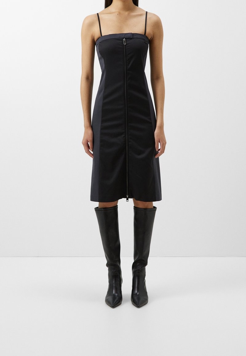 Sort ærmeløs kjole med lynlås foran, struktureret bodice og lige silhuet, parret med knæhøje sorte hæle støvler.