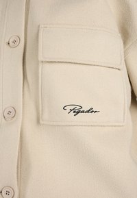 Giacca in pile color crema con chiusura a bottoni, una tasca sul petto e il logo ricamato "Pegador" in nero.