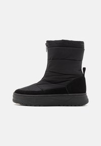 Bota de invierno negra de media pantorrilla con parte superior de nailon acolchado, acentos de ante, suela de goma gruesa, cremallera lateral y tirador en el talón.