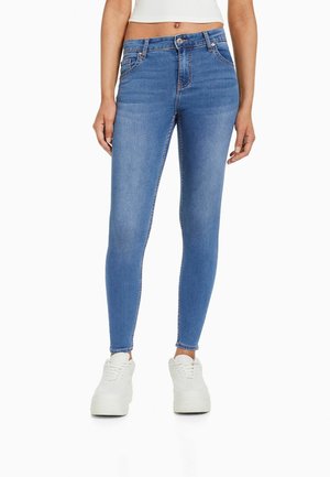 Jeans ajustados de color azul claro, hechos de denim, con una cintura de altura media, lazos para cinturón, bolsillos delanteros y traseros, y detalles de costura sutiles.