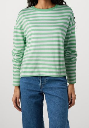 Grøn- og hvidstribet langærmet shirt med rund halsudskæring; blødt stof, afslappet pasform, båret sammen med blå lige-ben jeans.