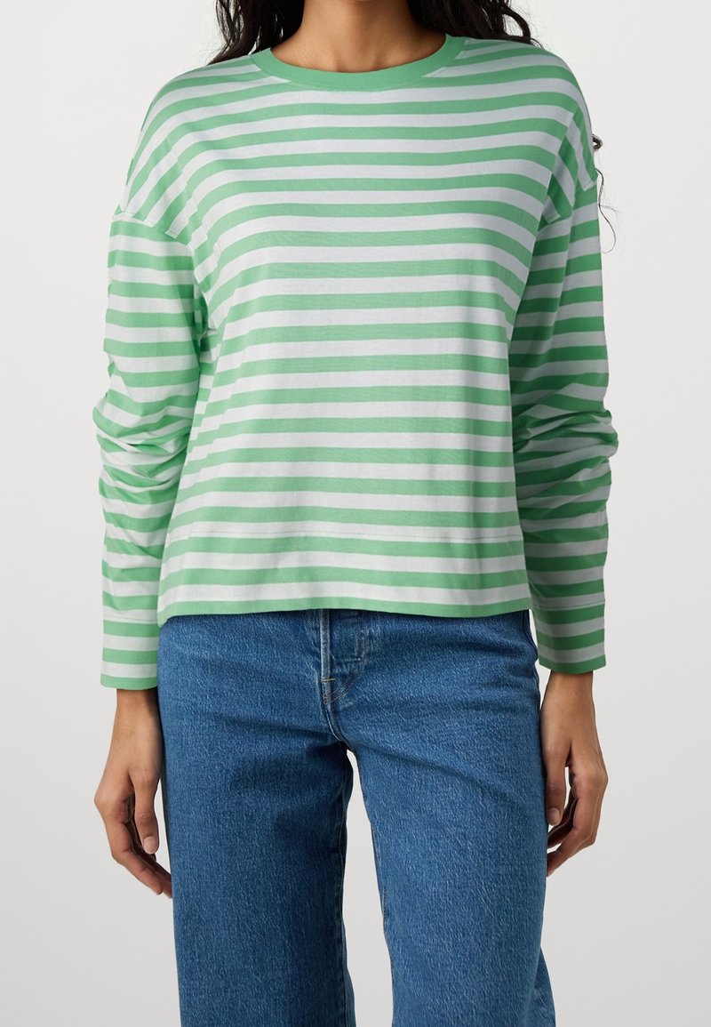 Grünes und weiß gestreiftes Langarmshirt mit Rundhalsausschnitt; weicher Stoff, lässiger Schnitt, getragen mit blauen geraden Jeans.