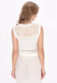 Witte gebreide mouwloze top met een boxy silhouet, open steekpatroon aan de achterkant en textuurribbel langs de randen.