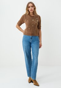 Bruine, fuzzy gebreide trui met korte mouwen en bloemenversieringen; gecombineerd met hoge, blauwe spijkerbroeken en bruine haklaarzen tot de enkel.