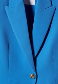 Blazer bleu vif avec de larges revers et un seul bouton décoratif doré fixé au centre devant.