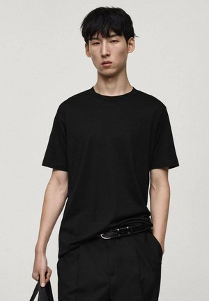Zwarte katoenen t-shirt met een klassieke ronde halslijn, korte mouwen en een ontspannen pasvorm, gecombineerd met zwarte broek en een zwarte riem.