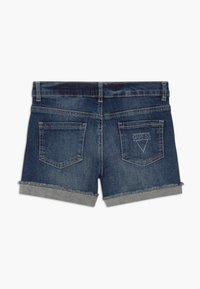 Pantalones cortos de mezclilla con un lavado azul oscuro, dobladillos deshilachados y un puño gris. Dos bolsillos traseros, uno adornado con piedras de strass en un patrón triangular.