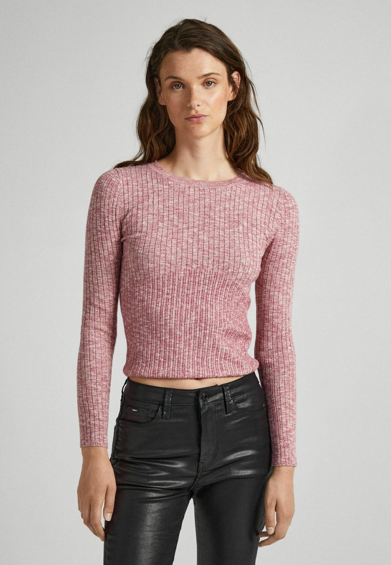 Maglietta a maniche lunghe a coste di colore rosa chiaro, realizzata in tessuto morbido. Presenta un collo a giro e un orlo leggermente accorciato. Abbinata a pantaloni neri.