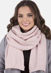 Écharpe rose clair en tissu doux, présentant une texture lisse et un design large et enroulé, drapée élégamment autour du cou de la personne qui la porte.
