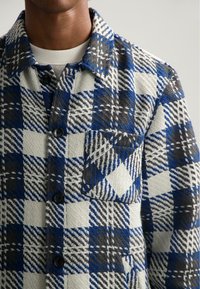 Geruite blouse met een blauw, grijs en wit kleurenschema, van textuurstof, met een knoopsluiting aan de voorkant en een borstzak.