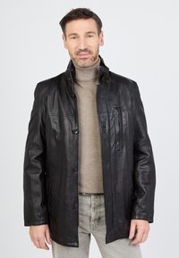 Schwarze Lederjacke mit einem Kragen, Knopfverschluss und zwei Fronttaschen. Verfügt über eine vertikale Reißverschluss-Tasche auf der linken Brust.