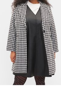Abrigo de espiga en blanco y negro con cuello de muesca, combinado con un vestido negro de cuero sintético y medias de rayas transparentes.