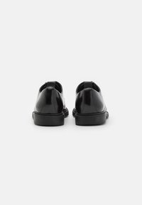 Un paio di scarpe eleganti in pelle verniciata nera mostrate dal tallone con maniglie sulla parte posteriore, su sfondo bianco.