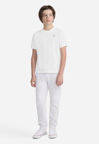 T-shirt en coton blanc à col rond, associé à un jogging en polaire gris clair et des baskets blanches avec des accents rouges et bleus.