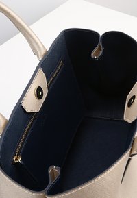 Guldtexturerad handväska med mörkblå foder, som har en dragkedja ficka och detaljer med magnetstängning. Rymlig design med dubbla handtag.