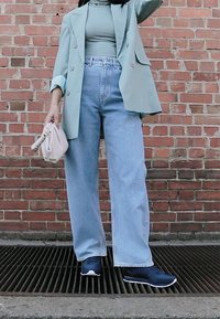 Myntgrønn oversized blazer, tettsittende tealkjole, høyt liv lys blå vide bukser og mørke sneakers. Kremfarget clutcher i hånden. Teglsteinsbakgrunn.