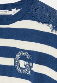 Gestreifter Pullover in Marineblau und Weiß, mit Spitzenakzenten an den Schultern, Fransenbesatz und einem strukturierten, mit R rhinestone verzierten "G"-Logo.