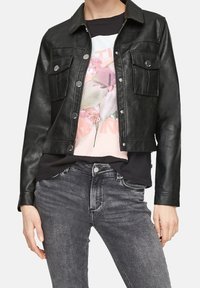 Chaqueta de cuero negra corta con dos bolsillos en el pecho y botones metálicos plateados, llevada sobre una camiseta gráfica de flores y combinada con pantalones vaqueros grises.