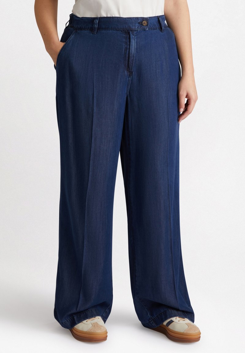 Weit geschnittene Jeanshose in Dunkelblau, mit Knopfverschluss, Seitentaschen und einer glatten Textur. Geeignet für Freizeitmode.