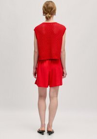 Rotes gestricktes ärmelloses Oberteil mit offenem Netzdesign, kombiniert mit passenden roten Shorts. Der Stoff hat eine glatte Textur und einen lockeren Schnitt.