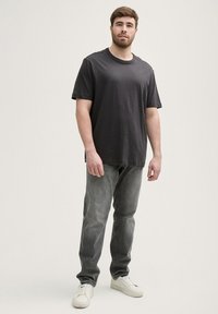 T-shirt en coton gris foncé avec un col rond, associé à un jean gris et des baskets blanches. Design simple avec des accents minimaux, coupe décontractée.