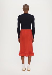 Navy long-sleeve top paired with a red satin skirt featuring a flounce hem. The look is completed with light socks and light clogs.