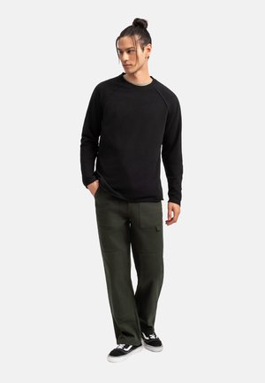 Felpa nera a maniche lunghe con girocollo abbinata a pantaloni cargo verdi, dotati di tasche e una vestibilità comoda, indossata con sneakers nere.