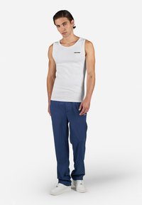 Witte mouwloze tanktop met een klein zwart logo, gecombineerd met blauwe pinstripe broeken en witte sneakers.