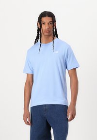 T-shirt en coton bleu clair à manches courtes et col rond. Présente un petit logo blanc sur la poitrine gauche. Alliée à un jean en denim foncé.