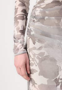 Dlhý rukáv šaty s kvetinovým vzorom v odtieňoch šedej a béžovej. Obsahujú nariasené detaily a elegantný, priliehavý strih.