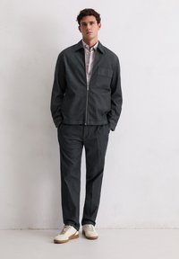 Ciemnoszara kurtka zapinana na zamek z kieszenią na klatce piersiowej, zestawiona z pasującymi spodniami i jasnymi trampkami. Gładka faktura na całej powierzchni.
