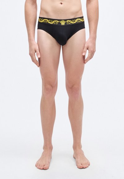 Culotte noire avec une ceinture ornementale dorée, présentant une coupe ajustée et une texture de tissu lisse. Aucun motif visible sur le corps de la culotte.