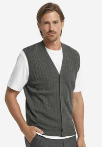 Grå ribbad stickad väst med V-ringning, med knappstängning framtill, bärs över en vit t-shirt. Mjuk textur och figurnära design.