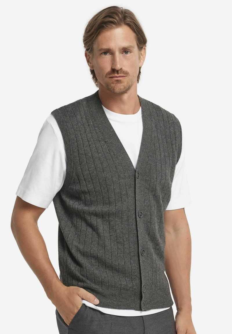 Grå ribbad stickad väst med V-ringning, med knappstängning framtill, bärs över en vit t-shirt. Mjuk textur och figurnära design.