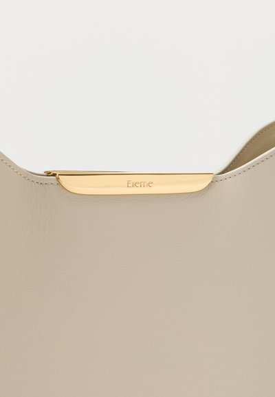 Λεπτομέρεια από μπεζ δερμάτινη τσάντα χειρός με χρυσό μεταλλικό κούμπωμα χαραγμένο με το όνομα της μάρκας "Ellene", που δείχνει ομαλή υφή και ακριβή ραφή.