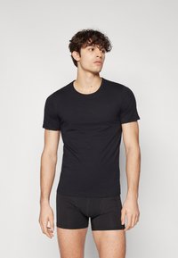 T-shirt noir à manches courtes en tissu doux avec un col rond. Design ajusté avec une texture lisse, associé à un short boxer noir ajusté.