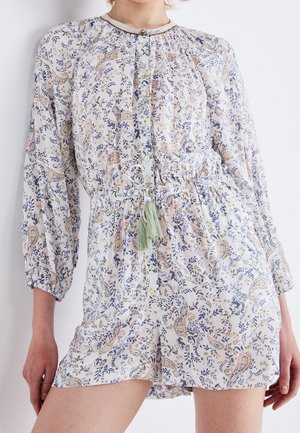 Květinový overal s dlouhým rukávem, zapínáním na knoflíky vpředu, staženým pasem a zelenou střapcovou šňůrkou na světle zbarvené látce, nošený stojící osobou.